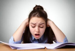 Image depicting a stressed student surrounded by textbooks and papers, symbolizing exam stress and academic pressure.